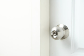 Silver doorknob on white wooden door of bathroom.