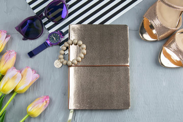 A gold notebook with women's shoes, tulips, glasses and a watch on a concrete background. Flet lay © Вася Фаевич