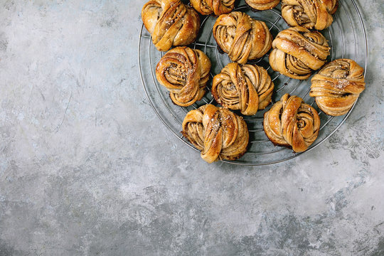 Traditional Swedish cardamom sweet buns Kanelbulle on cooling rack over grey concrete texture background. Flat lay, space