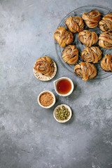 Traditional Swedish cardamom sweet buns Kanelbulle on cooling rack, ingredients in ceramic bowl above over grey concrete texture background. Flat lay, space