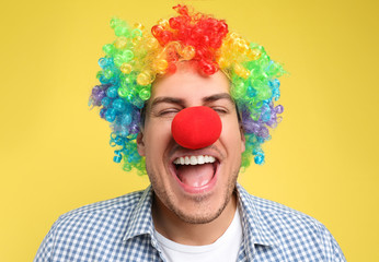Funny man with clown nose and rainbow wig on yellow background. April fool's day - obrazy, fototapety, plakaty