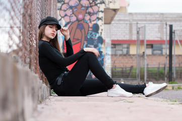 American portrait of young woman and long hair dressed in black clothes and leather jacket sitting and leaning on racks