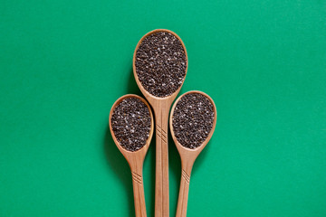 Chia seeds in wooden spoons. Superfood on a green background