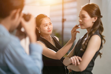behind the scene Asian makeup artist putting on more lipstick to the actress.