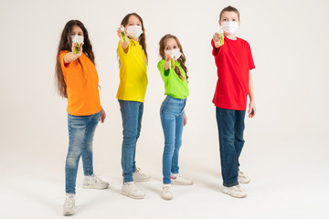 A group of schoolchildren in bright T-shirts and medical masks are holding disinfectants. Stay home and wash my hands. Coronavirus. Season of viral diseases