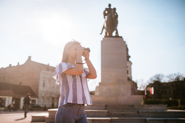  A young caucasian beautiful girl is taking a photo with a camera next to the monument