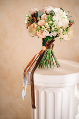 Classic autumn bridal bouquet made of white and orange flowers with brown ribbon on beige background close up.