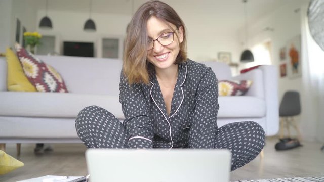 Smiling  Businesswoman dressed pajamas typing notebook keyboard chatting with friend sitting cross legged on living room floor office with laptop. Distance work in worldwide quarantine time 4K concept