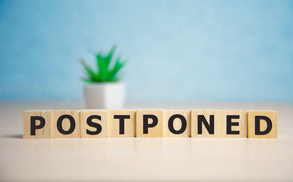 Postponed - words from wooden blocks with letters, postponed concept, top view background