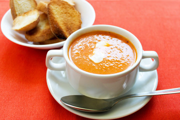 Tomato cream soup hot orange color close up view on bright red background. Selective focus. Copy space