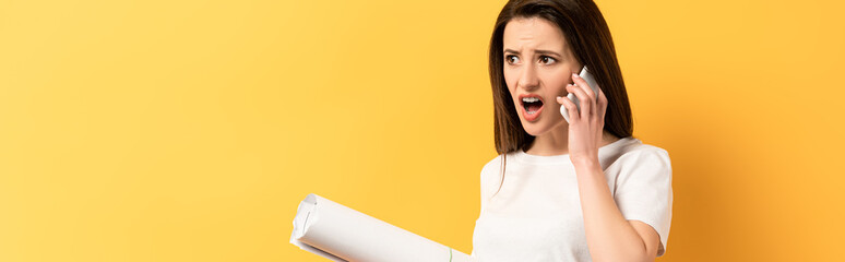 panoramic shot of shocked woman talking on smartphone and holding project on yellow background