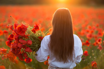 Little cute girl in white dress posing at field of poppies with a bouquet of poppies in her hands...