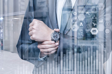 A businessman looks at the wristwatch on the background of a successful finance growth graph.