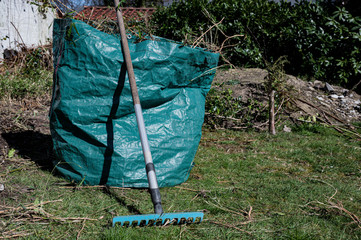 Eine Gartenharke steht vor einem Grünabfall Sack