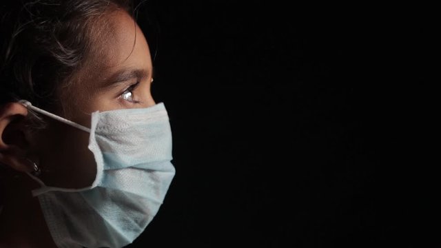 Young Girl With Medical Face Mask In Dark Room At Home Quarantine Due To Covid 19 Or Coronavirus Outbreak - Concept Of Hope And Fight To End Virus Crisis.