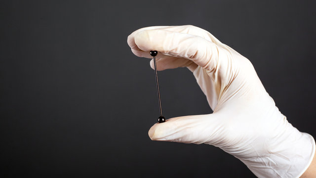 hand in a white sterile glove holds a piercing for cartilage ear jewelry on a dark background close-up