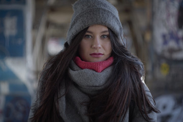 Portrait of beautiful brunette woman looking at camera. Young charming girl standing outdoors on city street in warm hat and scarf. Lifestyle.