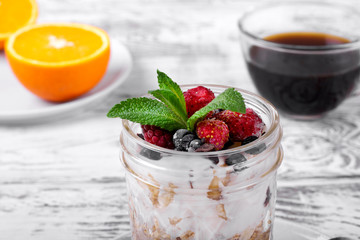 Overnight oats with yogurt topped with berries in a glass jar. Coffee and oranges in the background