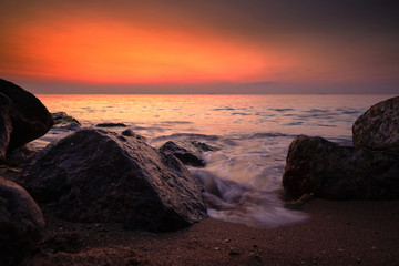 Sunrise at sea. Stones, waves and the sun. Seascape.