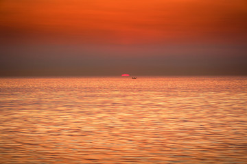 The boat is floating against the backdrop of the rising sun. Golden sunrise at sea.