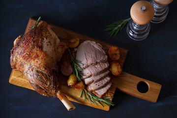 Roast leg of lamb with potatoes and rosemary on dark background. Overhead, flat lay, horizontal image
