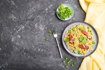 Quinoa porridge with green pea, corn and dried tomatoes on ceramic plate on a gray concrete background. Top view, copy space.