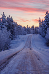 Obraz premium Winter scenery of a lonely icy road in Lapland at sundown, Finland