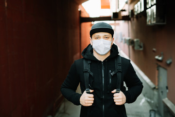 a young man in black sportswear and a baseball cap with a medical mask on his face near the red wall.