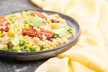 Quinoa porridge with green pea, corn and dried tomatoes on ceramic plate on a gray concrete background. Side view, selective focus.