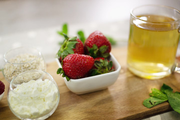 Food on a table with an eco napkin and on a cutting board, ready to prepare a healthy and tasty smoothie. Strawberries close-up, raspberries, protein, oats, mint green tea.