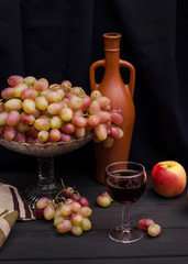 Red wine in a glass with grapes in a vase on a wooden table on a black cloth background with an old bottle. For wine advertising