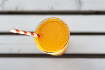 Appetizing thick orange color smoothie close-up with a red and white eco straw on a white wooden table.