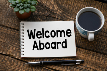 WELCOME ABOARD text inscribed in the notebook on a wooden table. © roobcio