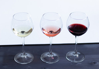 three glasses of different colors of wine on black wooden table and white wall background