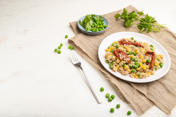 Quinoa porridge with green pea, corn and dried tomatoes on ceramic plate on a white wooden background. Side view, copy space.