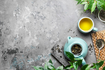 A cup of green tea in a blue cup on a gray concrete background. Cup of green tea with a teapot on a gray concrete background with copy space. Top view