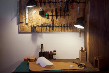 The room with wooden table and set of leather craft tools on it. Tools and leather at craftsman workplace. Leathermaker's workplace.