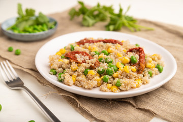 Quinoa porridge with green pea, corn and dried tomatoes on ceramic plate on a white wooden background. Side view, selective focus.