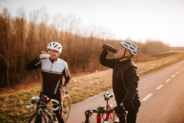  Two middle-aged cyclists drink water on the road. Resting