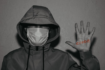 secret young man wearing jacket and medical mask with inscription: «COVID 19» on his hand...