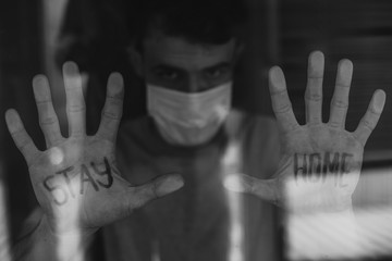 a young man looks out the window with the inscription: «STAY HOME»on the palm of his hand that is...