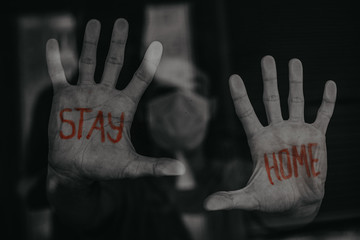 a young man looks out the window with the inscription: «STAY HOME»on the palm of his hand that is...