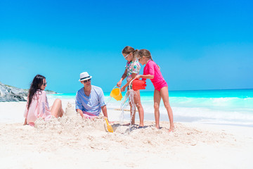 Family of four making sand castle at tropical white beach