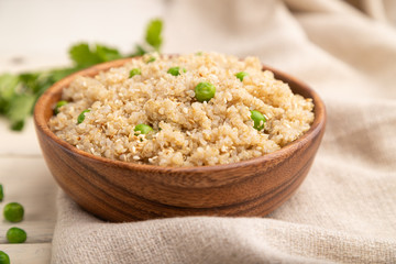 Quinoa porridge with green pea in wooden bowl on a white wooden background. Side view, selective focus.
