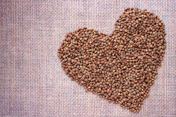 Heart-shaped bowl of roasted buckwheat on buckwheat background. Gluten free and healthy diet. I love buckwheat concept. Copy space