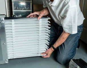 Senior caucasian man checking a clean folded air filter in the HVAC furnace system in basement of...