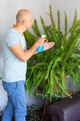 A man is spraying a fern from a spray bottle at home. © Albina
