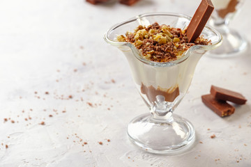 Delicate and delicious dessert. Cream cheese with chocolate and chopped nuts in a glass on a light background