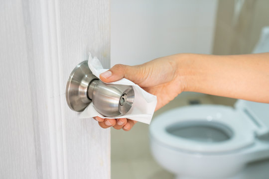 Close up of Asian woman hand using white toilet paper touch the public toilet door knob to prevent direct contact and prevent infection, virus, bacteria germs and dirt.