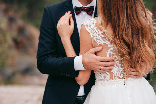 Groom In Black Suit And Bow Is Holding A Bride With Long Blonde Hair